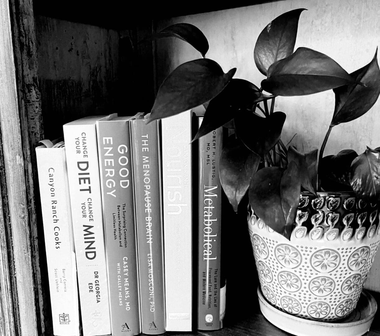 Books and a potted plant on a wooden shelf in black and white.