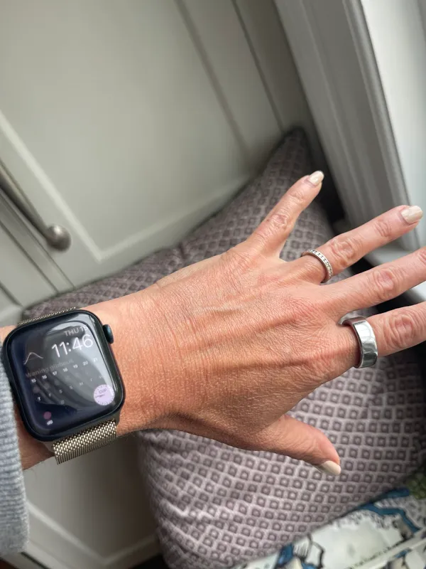 Close-up of a hand with rings and a smartwatch near a window.