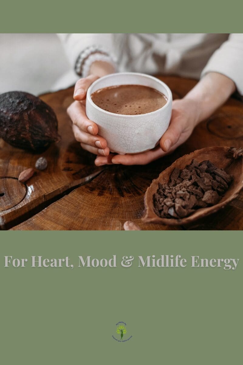 Hands holding a cup of cacao on a wooden table with cacao nibs — representing heart, mood, and midlife energy benefits.