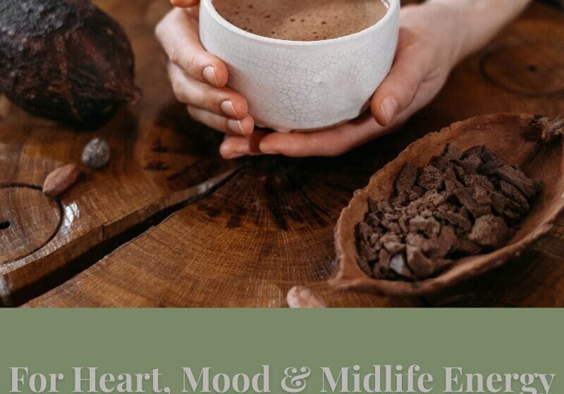 Hands holding a cup of cacao on a wooden table with cacao nibs — representing heart, mood, and midlife energy benefits.