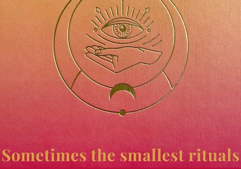 Close-up of a gradient pink and gold journal embossed with a hand and eye symbol, representing reflection, mindfulness, and personal insight — the journaling practice featured in My Midlife Mix.