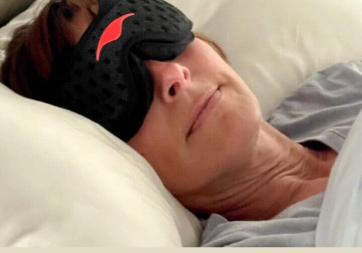 Woman resting in bed wearing a sleep mask, representing nighttime rest and midlife sleep support.