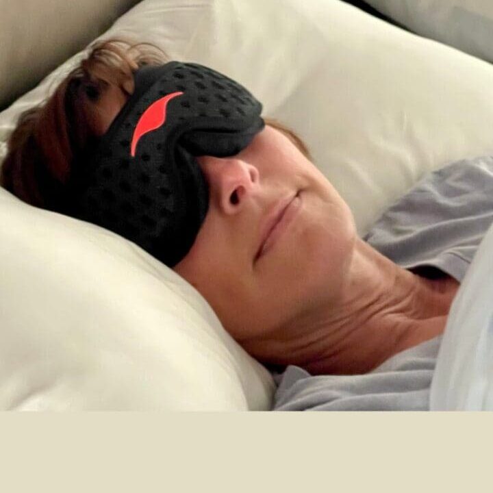 Woman resting in bed wearing a sleep mask, representing nighttime rest and midlife sleep support.